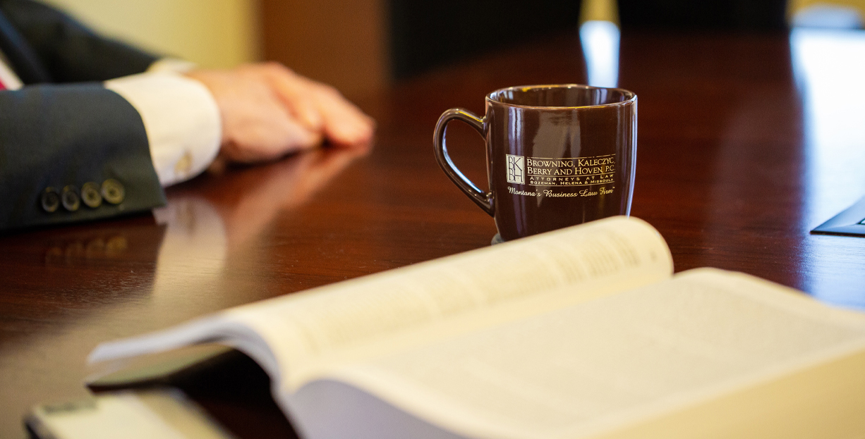 Open book, coffee cup, and hand on desk.